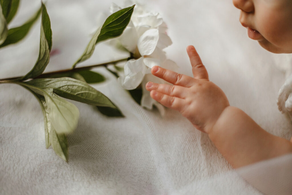 cute baby child hand and face with tender white peony lying white blanket